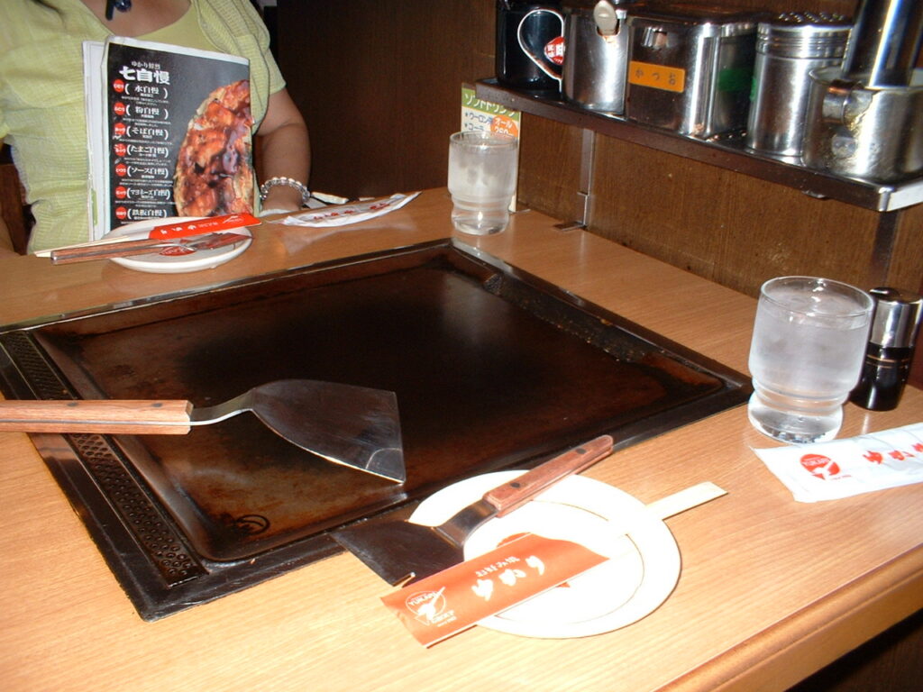 오코노미야키용 철판이 내장된 식탁에 놓인 넓은 금속 뒤집개와 접시